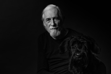 Black and white low key studio portrait of beautiful gray hair old man and his Big Black Schnauzer Dog. 