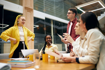 smiling leader of team standing with hands on the hips and waiting for her colleagues' report. young beautiful woman conducting servey among co-workers