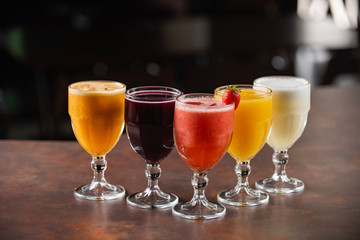 bowls of natural juices, passion fruit, grape, strawberry, orange, pineapple, on a table with dark background