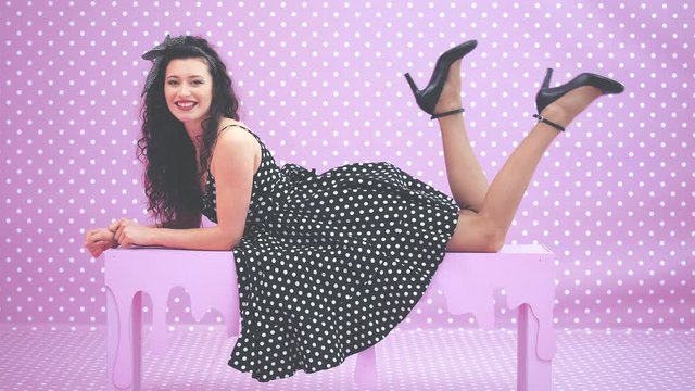 Enticing kinky brunnete girl in beautiful polka-dot dress lying on her belly on the bench moving flirtly her legs.