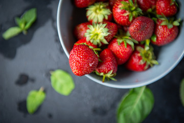 red ripe strawberries in a plate on a dark background top view