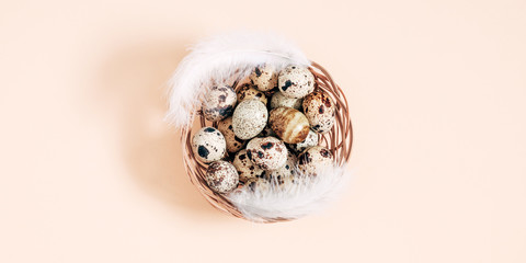 Quail eggs pattern, collection of quail eggs with feathers on beige background. Easter concept. Flat lay, top view, copy space