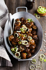 Mushrooms champignon fried in soy sauce, with pepper and steamed onions in an old metal bowl on an old vintage table. Selective focus.