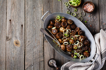 Mushrooms champignon fried in soy sauce, with pepper and steamed onions in an old metal bowl on an old vintage table. Selective focus.