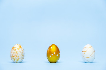 Three easter trendy golden decorated eggs on blue background. Happy Easter card with copy space for text Minimal easter style.