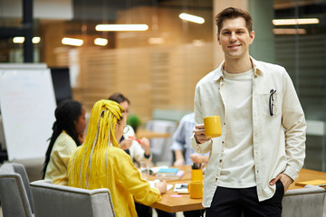 smiling cunning awesome man with a hand on his pocket flirting drinking tea, close up photo, guy having a rest while his colleagues are working on project, favourite job, profession, occupation
