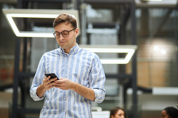 young clever man in glasses working with cell phone. low angle view . gadget, guy briwsing the net,...