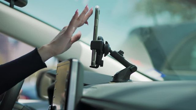 A woman texts on her phone attached to the dash while in her car