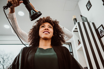 Beautiful latin woman with short curly brown hair getting a treat at the hairdresser. Latin hairdresser working her afro hair. Lifestyle