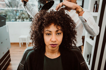 Beautiful latin woman with short curly brown hair getting a treat at the hairdresser. Latin...