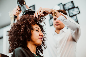 Beautiful latin woman with short curly brown hair getting a treat at the hairdresser. Latin hairdresser working her afro hair. Lifestyle
