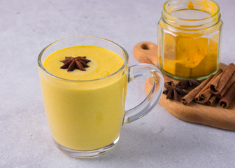 Golden milk with turmeric and other spices - a traditional Ayurvedic drink stands in a glass cup.