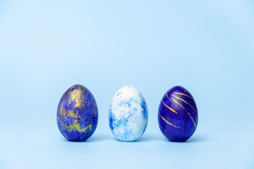 Three easter trendy colored classic blue, white and golden decorated eggs on blue. Happy Easter card with copy space for text. Minimal style