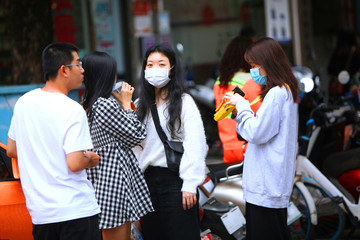 Naklejka na ściany i meble Chinese youth stand on the street in gauze masks on their faces, talking and drinking drinks. The threat of a coronavirus epidemic in China. Copy space.