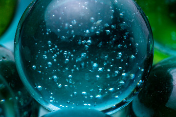 Super close up macro shot of a glass marble with bubbles reflecting in the transparent teal blue coloured smooth surfaced stone resting on top of other crystals