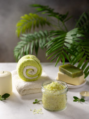 spa background with sea salt, solid soap, candles and bath towels on a background of green palm leaves. Healthy relaxation, therapy and treatment. copy space. vertical image