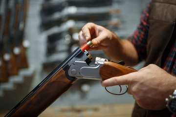 Man loads a rifle, gun shop interior on background