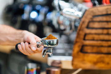 Detail of man hand holding portafilter recipient filled with coffee ground while preparing espresso