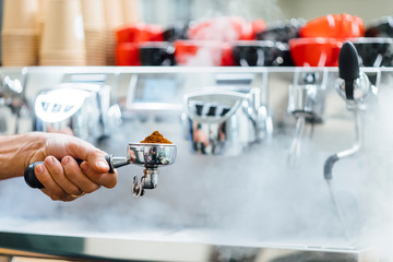 Detail of man hand holding portafilter recipient filled with coffee ground while preparing espresso