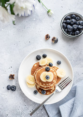 pancakes with fresh blueberries, banana on a gray background with white flowers. healthy breakfast. vertical image, top view