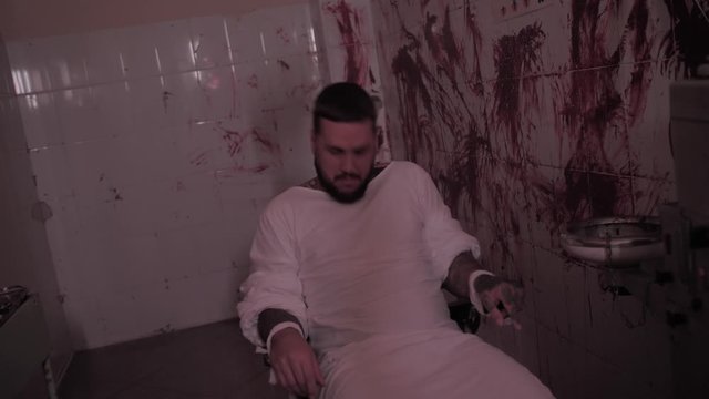 Crazy man in straitjacket tied to a chair, killer psychopath in a room with bloodied walls overdose