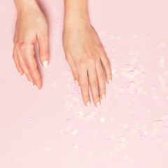 Obraz na płótnie Canvas Stylish fashionable female manicure in pastel colors. Hands of young girl on pink background with festive confetti. Minimalist manicure trend. Flat lay, top view, copy space. Natural nails, gel polish