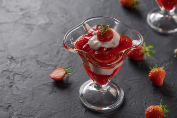 Cream dessert with fresh strawberries and strawberry jam in a glass bowl on a dark background