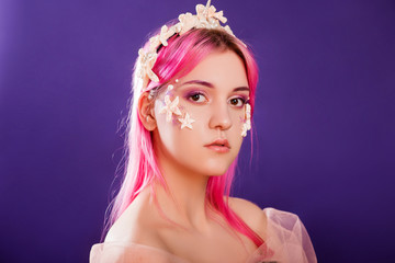 Close up portrait of a young beautiful girl with pink hair and professional make-up, sea princess with starfish and shells on her face and head. Halloween makeup.