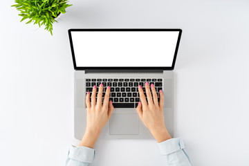 Woman’s hands working on laptop with empty screen on white background. Office desktop with accessories. Top view