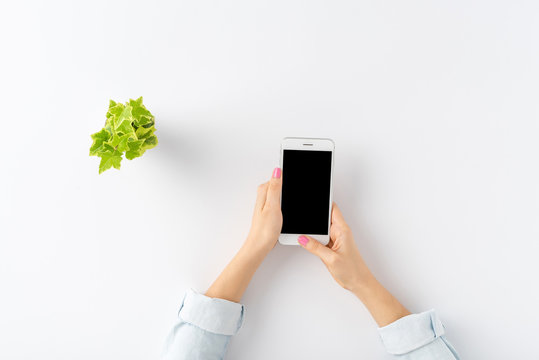 Woman’s Hands Using Mobile Phone With Empty Screen On White Table. Office Desktop Concept. Top View