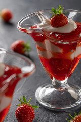 Cream dessert with fresh strawberries and strawberry jam in a glass bowl on a dark background