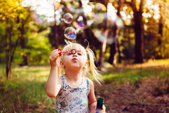 Funny little girl blowing soap bubbles in summer