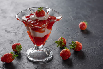 Cream dessert with fresh strawberries and strawberry jam in a glass bowl on a dark background