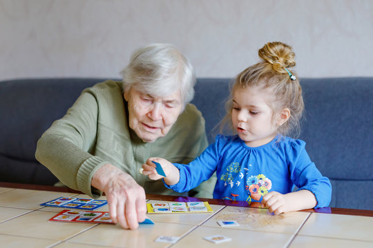 Beautiful toddler girl and grand grandmother playing together pictures lotto table cards game at home. Cute child and senior woman having fun together. Happy family indoors