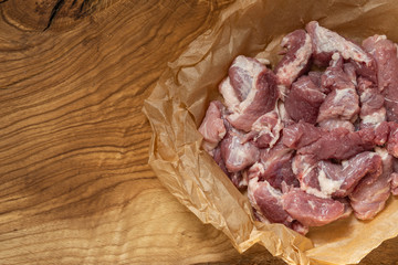 A piece of pork cut into pieces on paper lies on a wooden surface