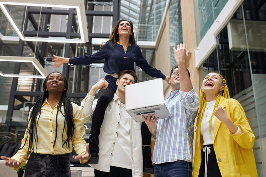 Group of happy workers screaming with pleausure, pretty lovely woman sitting on the shoulder of man and expressing trumph, happiness