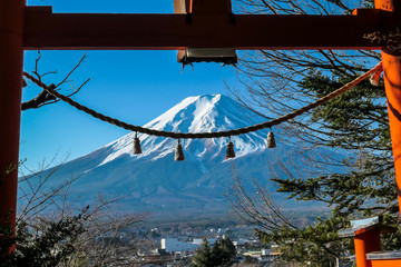 Distant view on Mt Fuji, framed in between orange Torri gate, decorated with bells,  on a clear, wintery day. The top parts of the volcano are covered with a layer of snow. Holly mountain