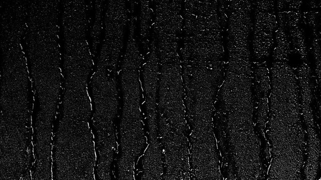 Rain water droplets slowly trickling down the window pane at night