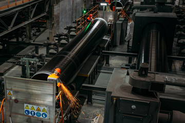 Male workers grinding butt weld pipe in metalwork workshop