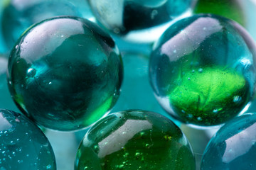 Close up macro shot of a group of marbles. Glass spheres with bubbles reflecting in the transparent teal blue coloured smooth surfaced stones.