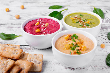 Colorful hummus in the white bowls on the white wooden table. Classic, beetroot and spinach chickpea dips