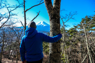 A man standing in a forest on the hilltop above Chureito Pagoda, Japan with Mt Fuji in the back. He...