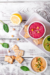 Colorful hummus in the white bowls on the white wooden table. Classic, beetroot and spinach chickpea dips