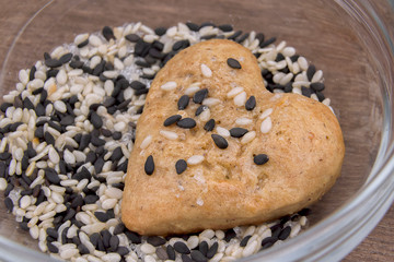 Gingerbread cookie hearts in a transparent glass bowl on a wooden table. The scene of making sweet homemade pastries with black and white sesame, sugar. Rustic style recipe