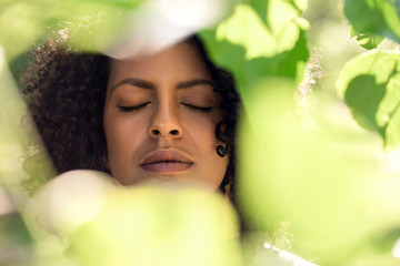 Young woman with her eyes closed framed by green leaves