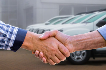 Businessmen sign a deal to sell a car with a handshake. Handshake of men on cars background_