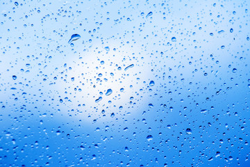 Wet glass with rain drops on blue sky background_