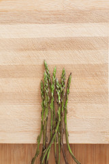 Close up of a bunch of asparagus on top of a wooden surface with even, warm light.