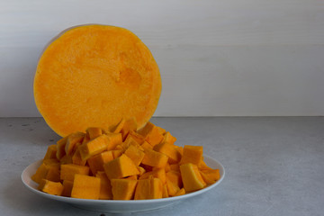 Pumpkin cubes on a plate and a round slice of fresh pumpkin on a grey background.