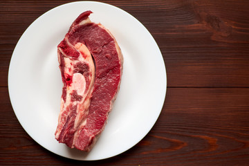 Raw veal steak on a white plate on a wooden background.